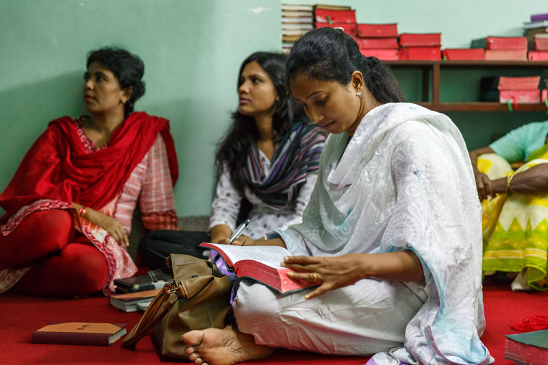 Asia women seated on the ground listening to a message with an open Bible