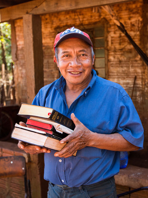 Latino man holding a stack of Bibles.